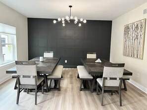A dining area with a dark wooden table, grey upholstered chairs, and a modern chandelier.