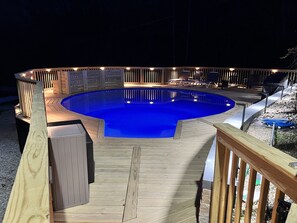Ein runder Pool mit Holzterrasse und Beleuchtung.