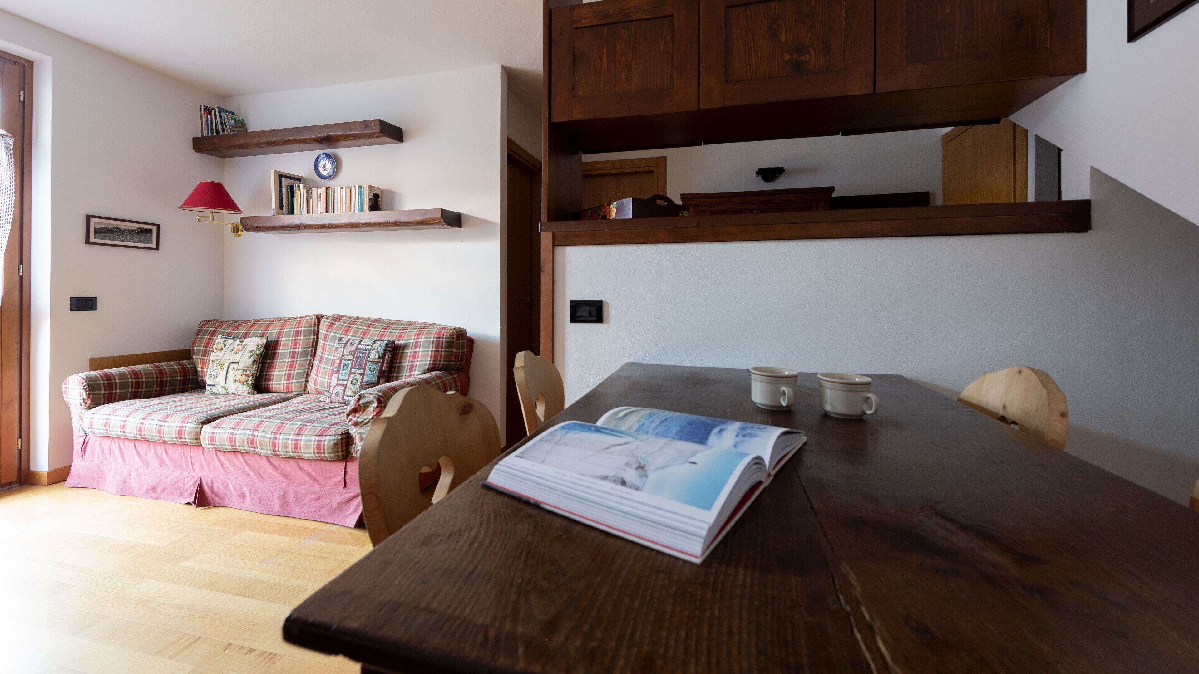 A cozy living room with a sofa, a wooden dining table, and a bookshelf.