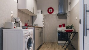 A compact kitchen with a washing machine, a coffee maker, a microwave, and a small stove. - Monastiraki Psiri, 1-bedrom apartment, sleep 2-4p, Old Town, Great Court Yard. (Athina)