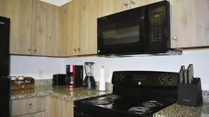 Una cocina con gabinetes de madera, un microondas negro, una estufa, una cafetera y una licuadora.