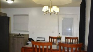 Un comedor con una mesa y sillas, una araña y una cocina al fondo.