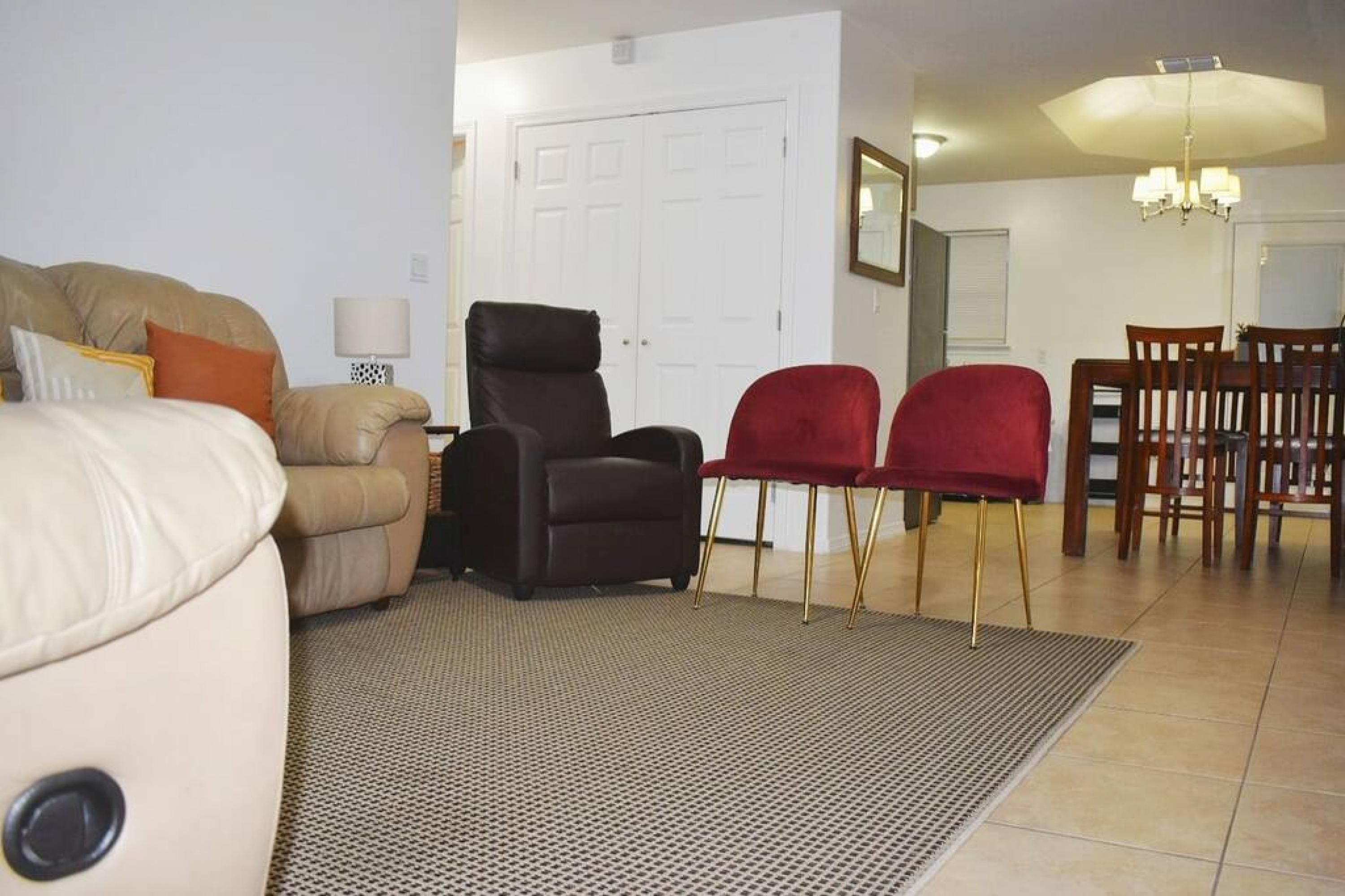 Een woonkamer met een beige bank, een zwarte fauteuil en twee rode stoelen. Achtergrond is een eettafel met stoelen.