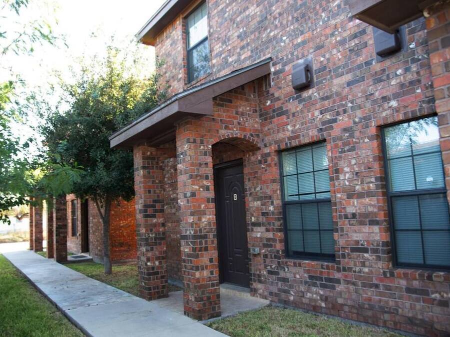 Un edificio de ladrillo con puerta negra, ventanas con contraventanas y un corredor cubierto.