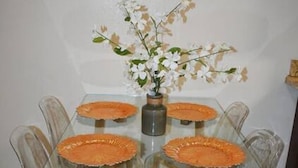 Et spisebord med glasplade, fire stole, en vase med blomster og et flisegulv.