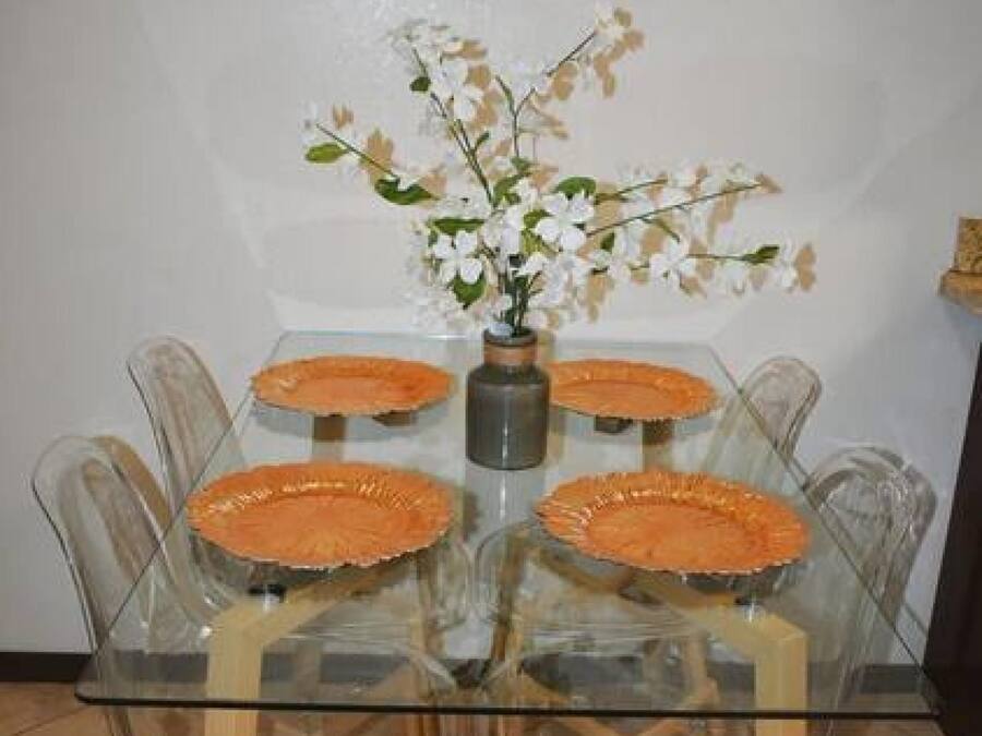 Una mesa de comedor con cubierta de vidrio, cuatro sillas, un florero con flores y un piso de baldosas.