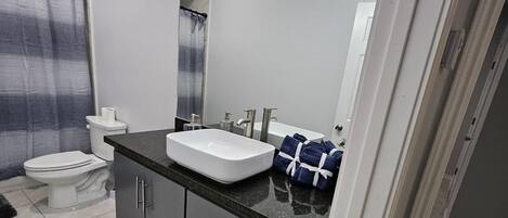 A modern bathroom with a white sink, dark cabinets, and a black rug.