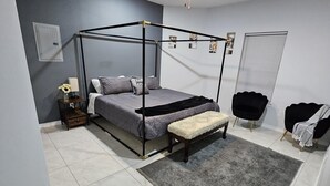 Un dormitorio moderno con cama de dos plazas, ventilador de techo, mesita de noche con lámpara, un banco y una silla.