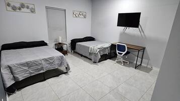 A bedroom with a bed, a desk, a chair, a ceiling fan, and a TV mounted on the wall.