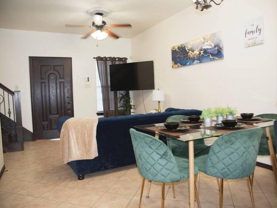 A dining area with a glass table and teal chairs, a dark blue sofa, and a ceiling fan.