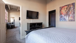 A hotel room with a large bed, a flat-screen TV mounted on the wall, a painting on the wall, and a desk with a chair. - Beautiful Downtown Condo "Unbeatable Location" with Secure Onsite Parking (New Orleans)