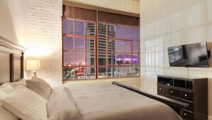 A hotel room with a large bed, a TV, a window with a city view, and a wooden cabinet.