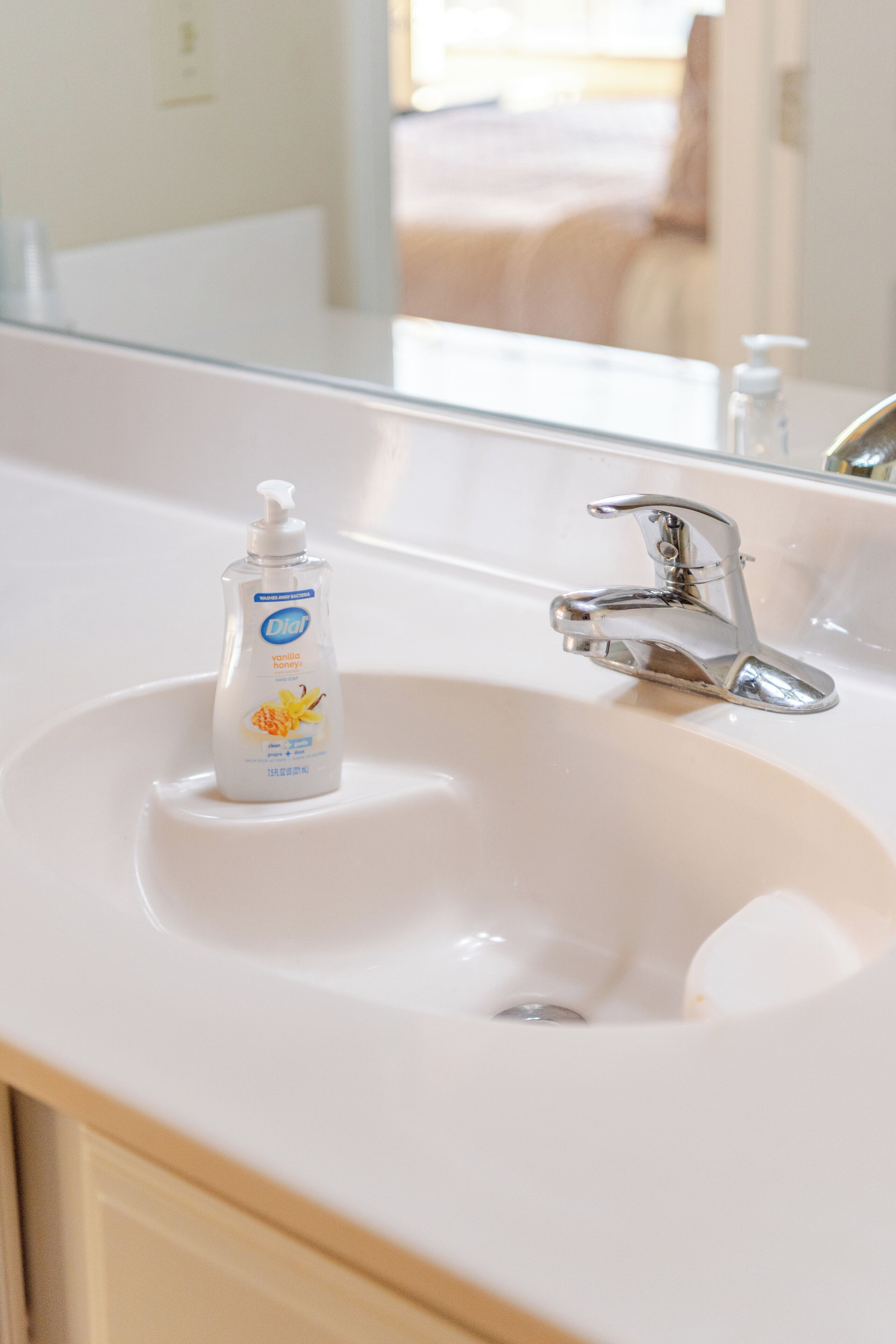 A bathroom with a white sink, a chrome faucet, and a bottle of DKT honey-scented soap.