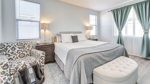 Een slaapkamer met een bed, nachtkastjes, een lamp, een stoel en een raam met gordijnen.