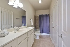 Un baño con lavamanos doble, inodoro, ducha con cortina y un espejo grande.