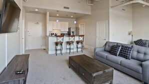 Un salón espacioso con un sofá gris, una mesa de centro de madera y una cocina al fondo.