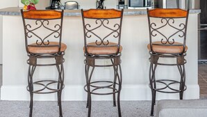 Una cocina con tres taburetes de bar, un microondas, un refrigerador y una cafetera.