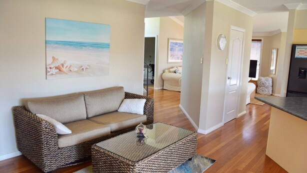 A living room with a sofa, coffee table, and a painting of a beach scene. - Pete's Place. Well-appointed reburnished 2 storey house (South West Rocks)