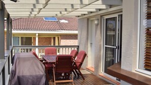 A covered outdoor patio with a table and chairs, a solar panel, and a view of a brick building. - Pete's Place. Well-appointed reburnished 2 storey house (South West Rocks)