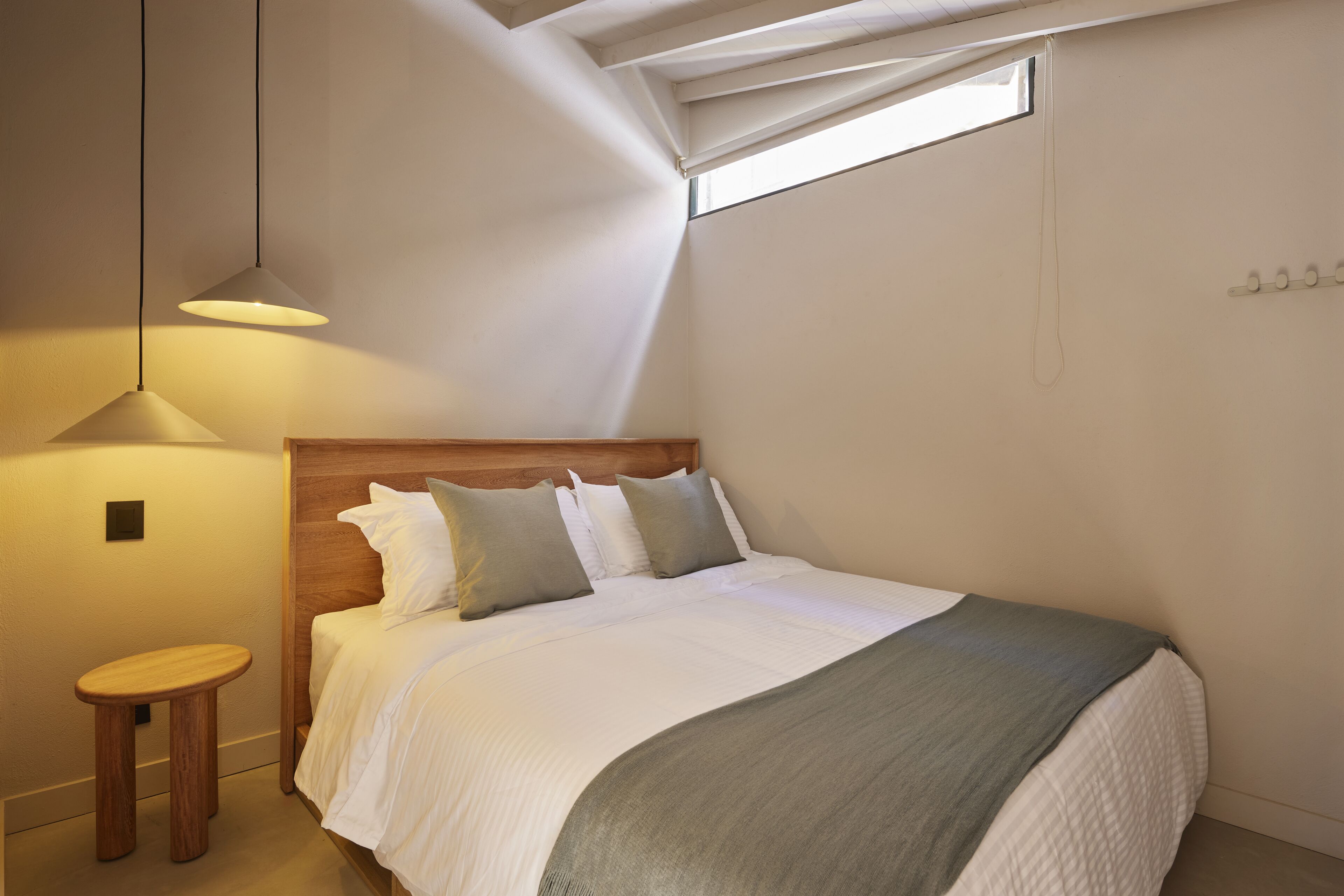 A bedroom with a bed, a wooden headboard, a small stool, a window, and a pendant light.