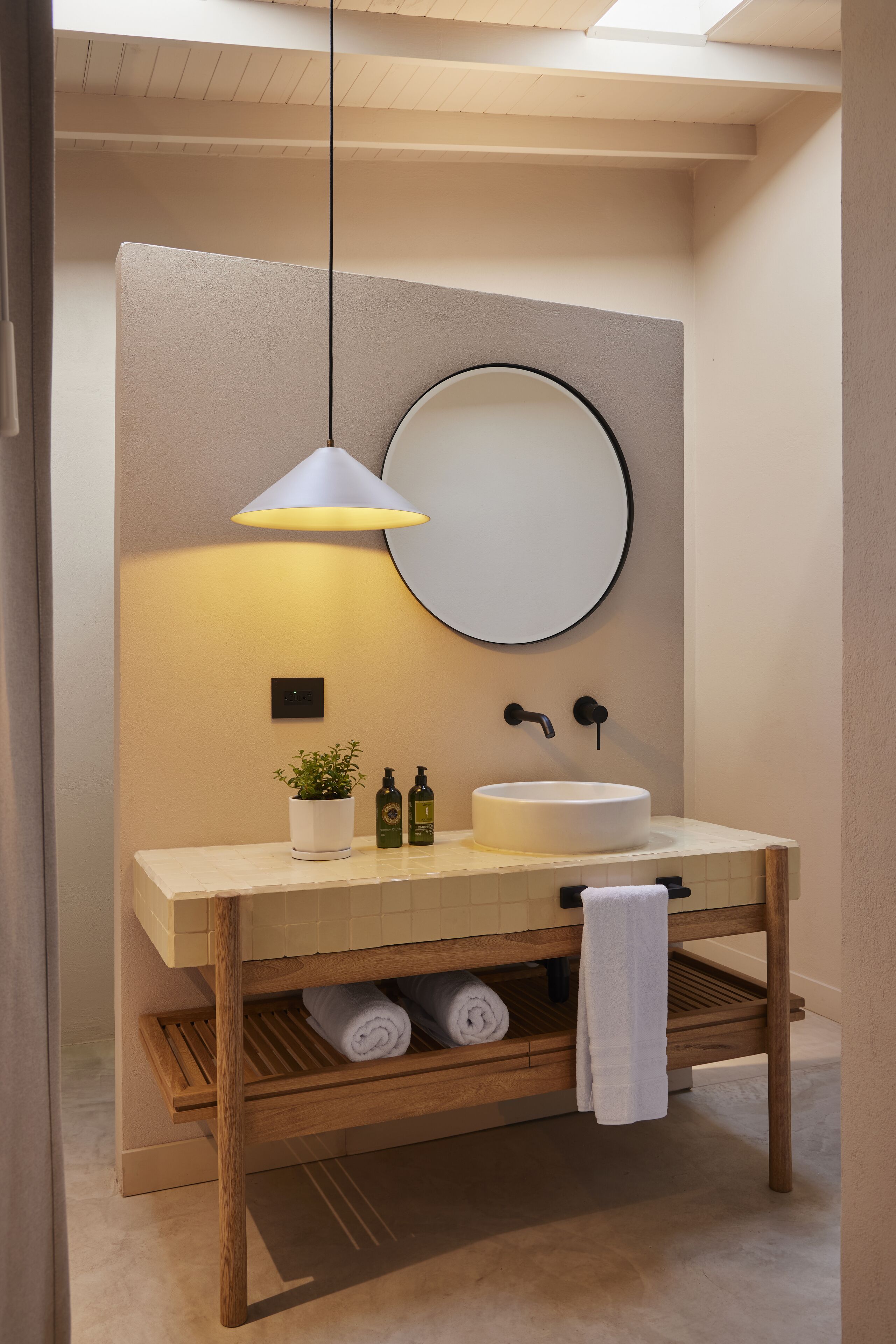 Un baño moderno con un espejo redondo, un lavabo blanco y un tocador de madera.