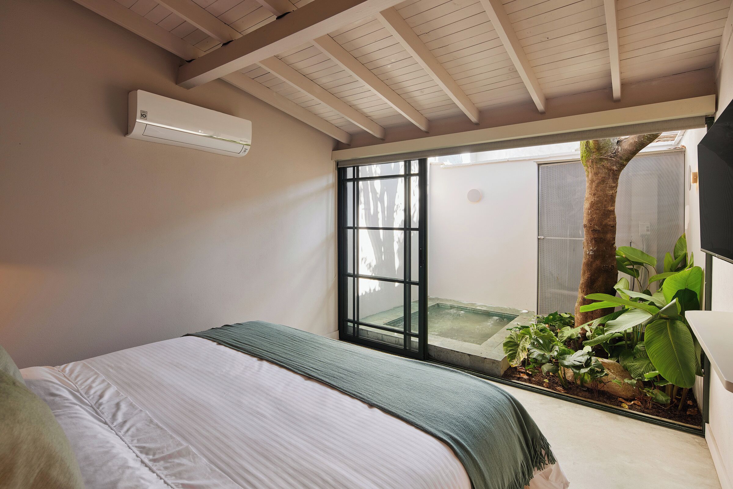 Un dormitorio con una cama, un ventanal corredero que da a un balcón y un pequeño jardín interior.