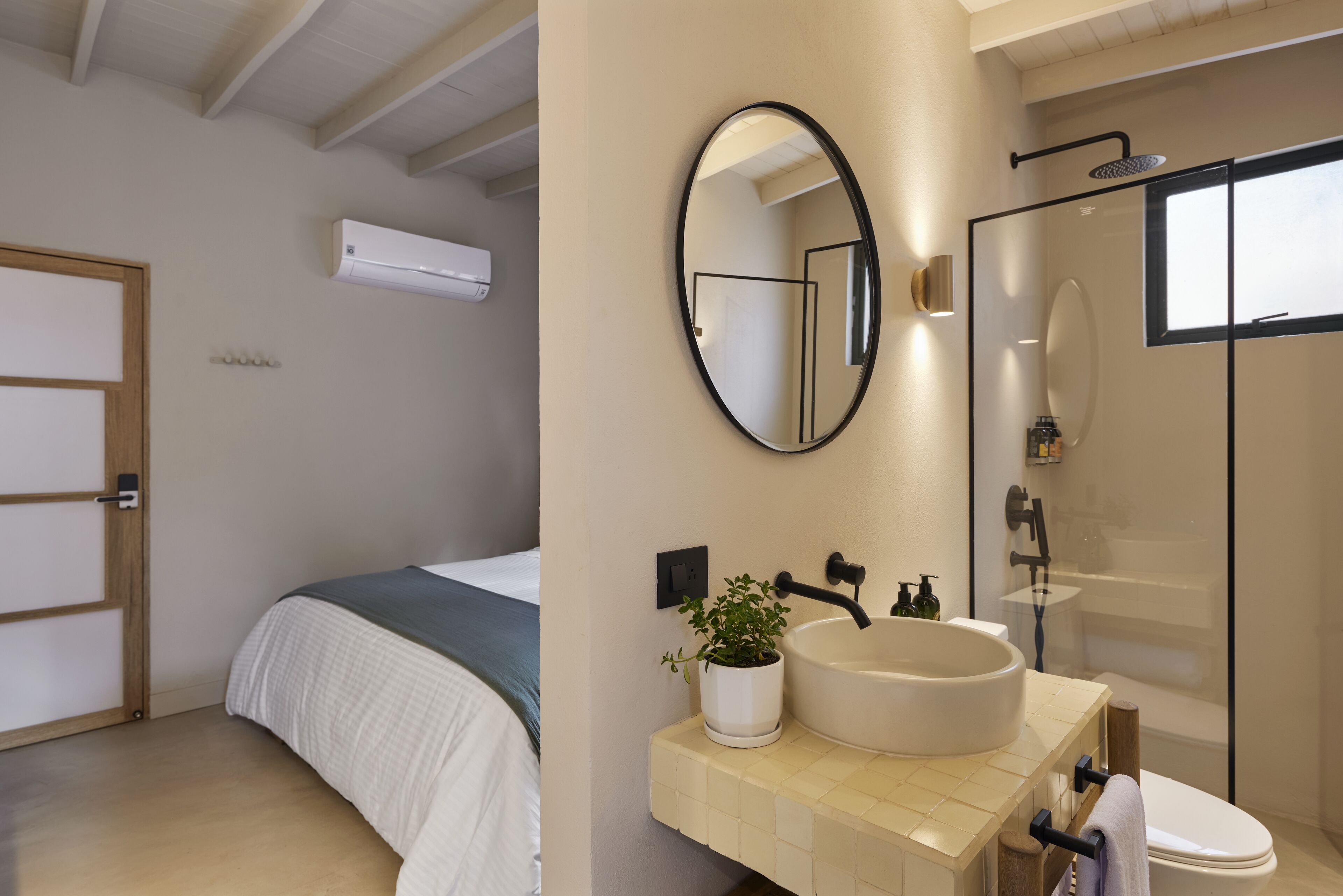 Een moderne slaapkamer met een bed, een badkamer met wastafel, spiegel en douche.