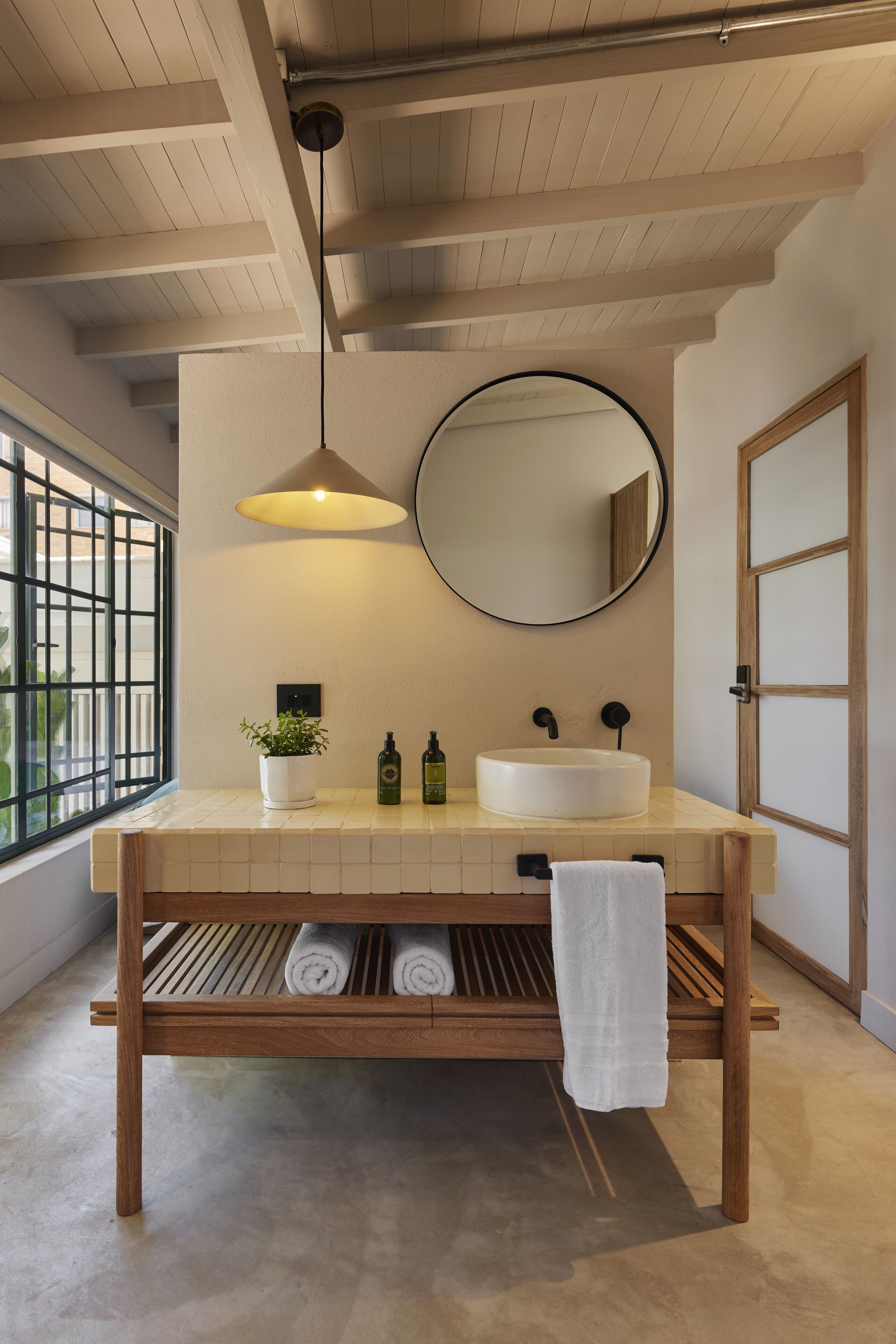 A modern bathroom with a wooden vanity, a round mirror, and a pendant light.