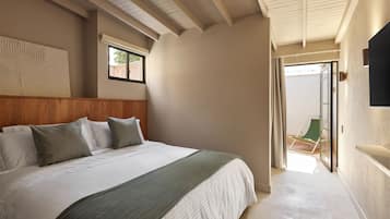 Ein Schlafzimmer mit einem großen Bett, einem hölzernen Kopfteil, einer grünen Tagesdecke und Blick ins Freie durch eine Schiebetür.