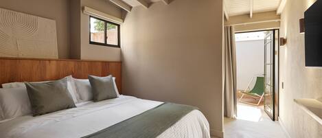A bedroom with a large bed, a wooden headboard, a green throw blanket, and a view of the outdoors through a sliding door.