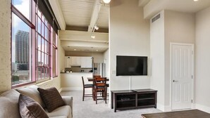 Ein Wohnzimmer mit einer Couch, einem Couchtisch und einem Fernseher. Es gibt einen Essbereich mit Tisch und Stühlen.