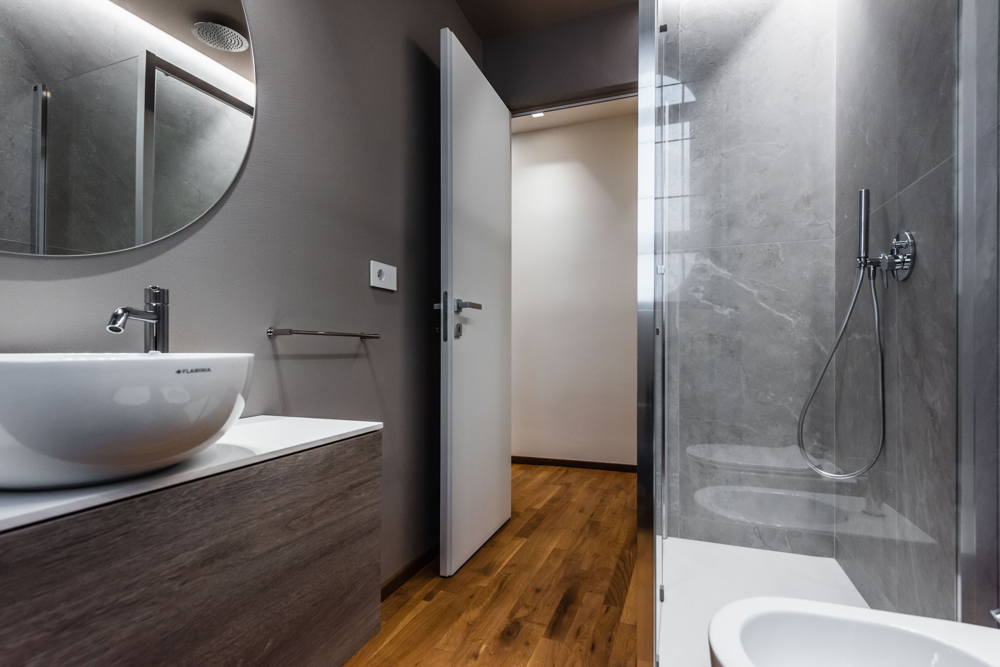 Un baño moderno con un espejo grande, un lavamanos blanco y una zona de ducha.
