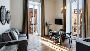 En moderne stue med sofa, spisebord, stole, store vinduer med gardiner og et fladskærms-tv.