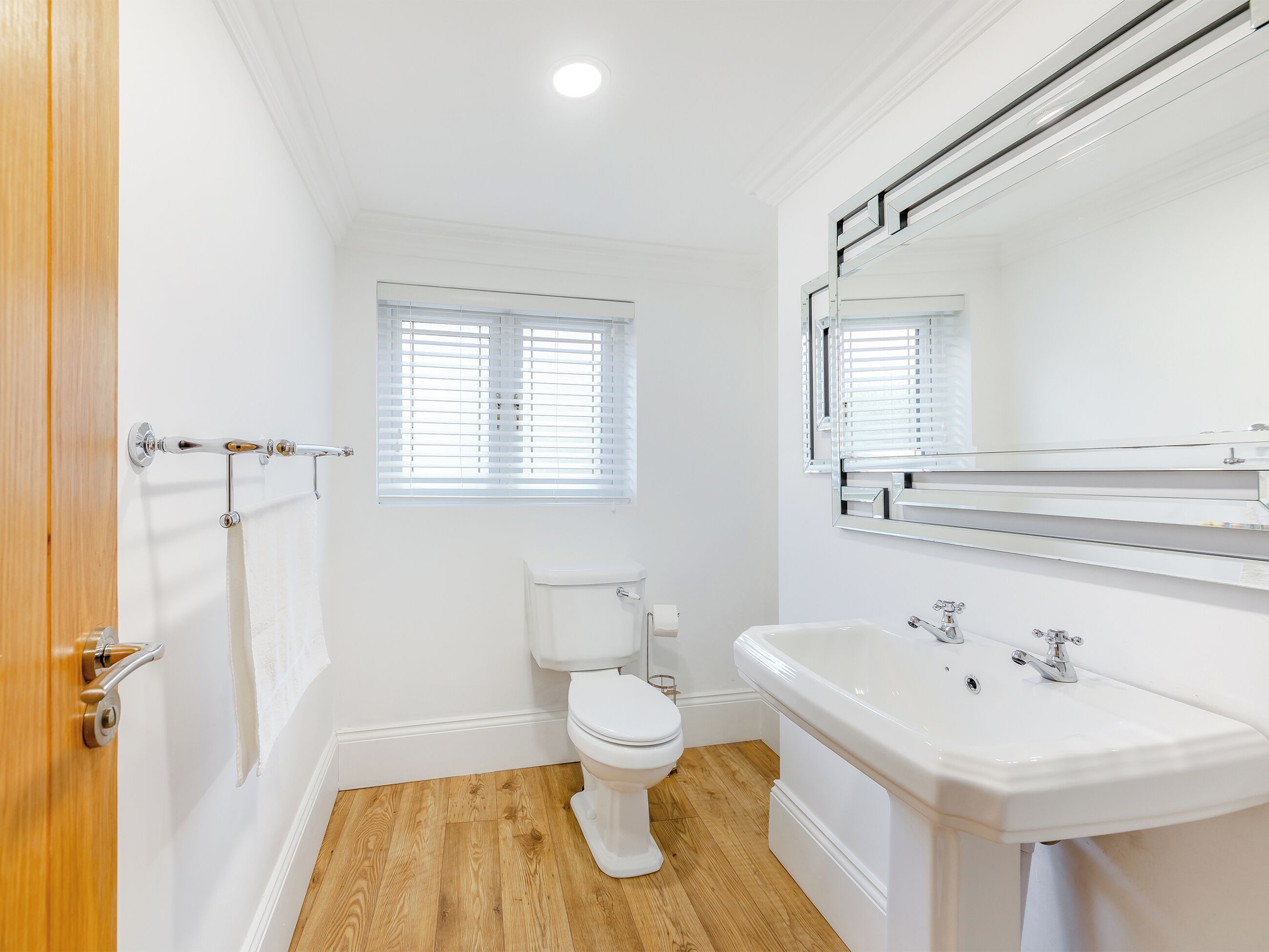 Une salle de bain avec des toilettes, un lavabo et une fenêtre avec des stores.