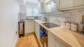 A compact kitchen with a built-in microwave, toaster, and a dishwasher. It features light-colored cabinets, a wooden countertop, and a window with blinds.