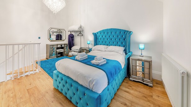 A bedroom with a large bed, a chandelier, a dresser, and a mirror.