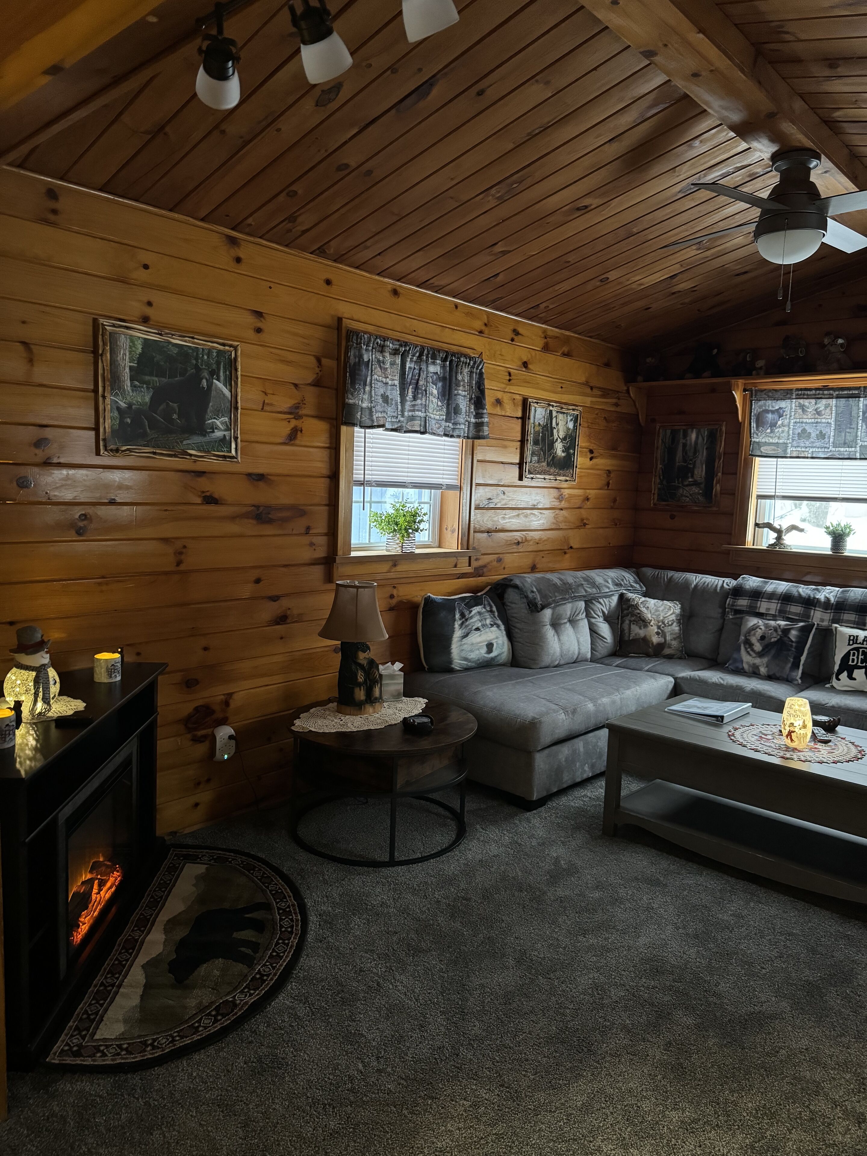 A cozy cabin interior with a fireplace, a gray sofa, a coffee table, and wooden walls.