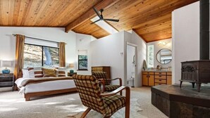 Une chambre avec un grand lit, un plafond en bois, une cheminée et une vue sur l’extérieur.