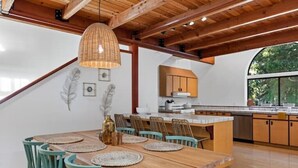 Un coin repas avec une table et des chaises en bois, un luminaire suspendu et une cuisine en arrière-plan.