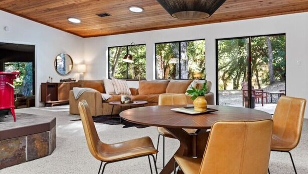 Un salon moderne avec un plafond en bois, de grandes fenêtres, une table à manger ronde et des meubles en cuir.