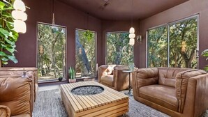 Un salon moderne avec des canapés en cuir, une table basse en bois et de grandes fenêtres donnant sur la verdure.