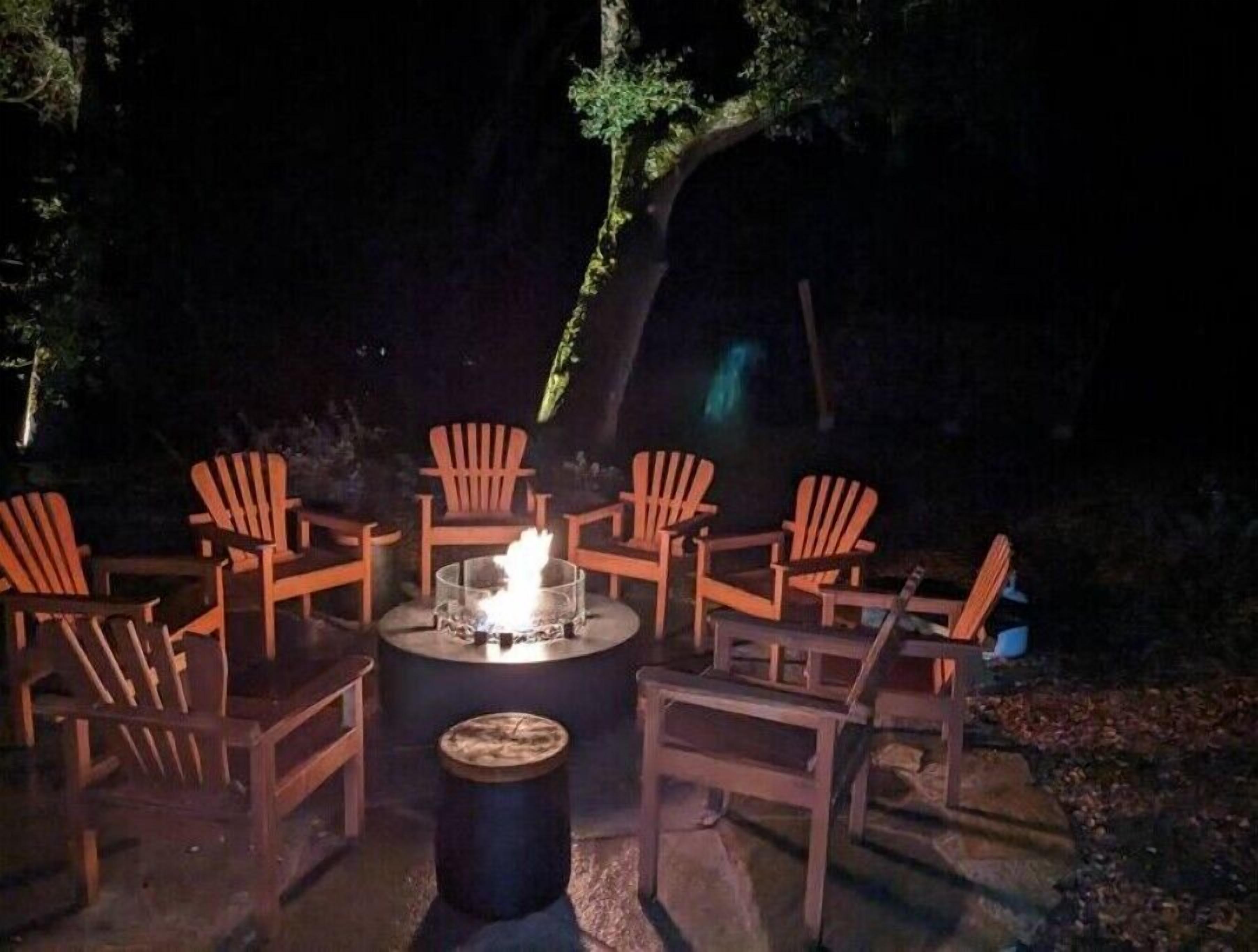 Un espace extérieur aménagé avec des chaises Adirondack en bois disposées autour d’un foyer circulaire.