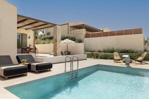Un espace piscine comprenant des chaises longues, une table et un pilier en pierre.