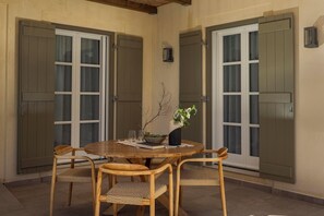 Un coin repas avec une table ronde en bois, quatre chaises en osier et un vase agrémenté de quelques plantes vertes.