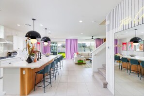 A modern kitchen with a central island, bar stools, and pendant lighting. - 7BR Pickleball: Firepit-Outdoor Kitchen-Game Room (Coachella)