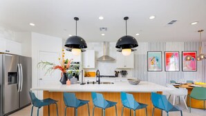 Une cuisine moderne dotée d’un îlot central, de tabourets de bar, d’appareils électroménagers en acier inoxydable et d’un éclairage contemporain.