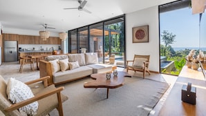 A modern open-plan living area with a kitchen, seating arrangements, and a large sliding glass door leading to a balcony with a view of the sea. - Brand-new luxury Villa Element (Provincia de Puntarenas)