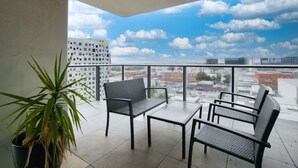 A balcony with a view of the city, a potted plant, and two chairs and a table. - Pokemon Inspired Apt -Pool-Gym-Sauna-Steam Room (Adelaide)