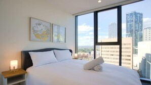 A hotel room with a large bed, a nightstand, and a window with a city view. - Paradise 2BR Apt in Rundle Mall (Adelaide)