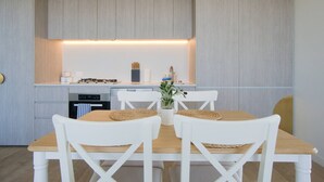 A compact kitchen with modern appliances, a dining table with white chairs, and a small island with a plant.